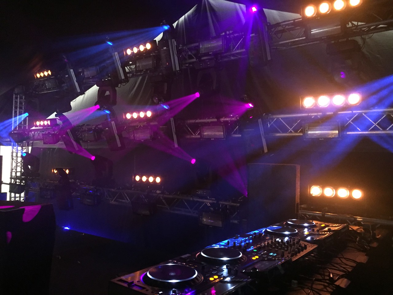 Lights with beams in haze behind a DJ deck